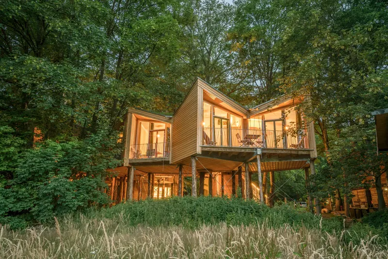 Baumhaus aus Holz mit großen Fenstern im dichten Wald, innen warm beleuchtet